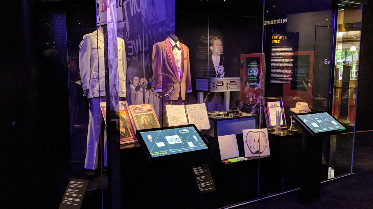 Australian music vault museum exhibition Diverse range of clothes, books and images behind glass case.