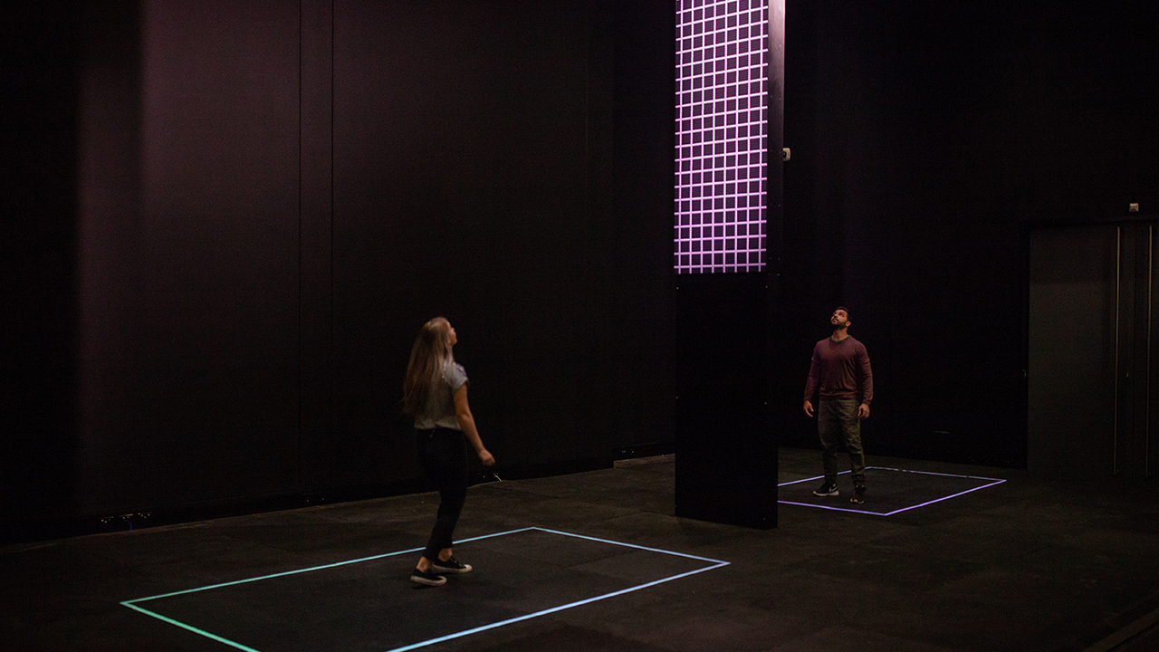 Long shot of Cascade exhibition, man and woman watch screen.