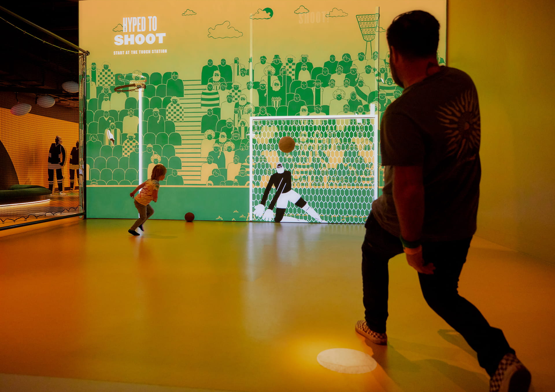 Interactive soccer experience Man and child kicking a soccer ball at animated goalie.