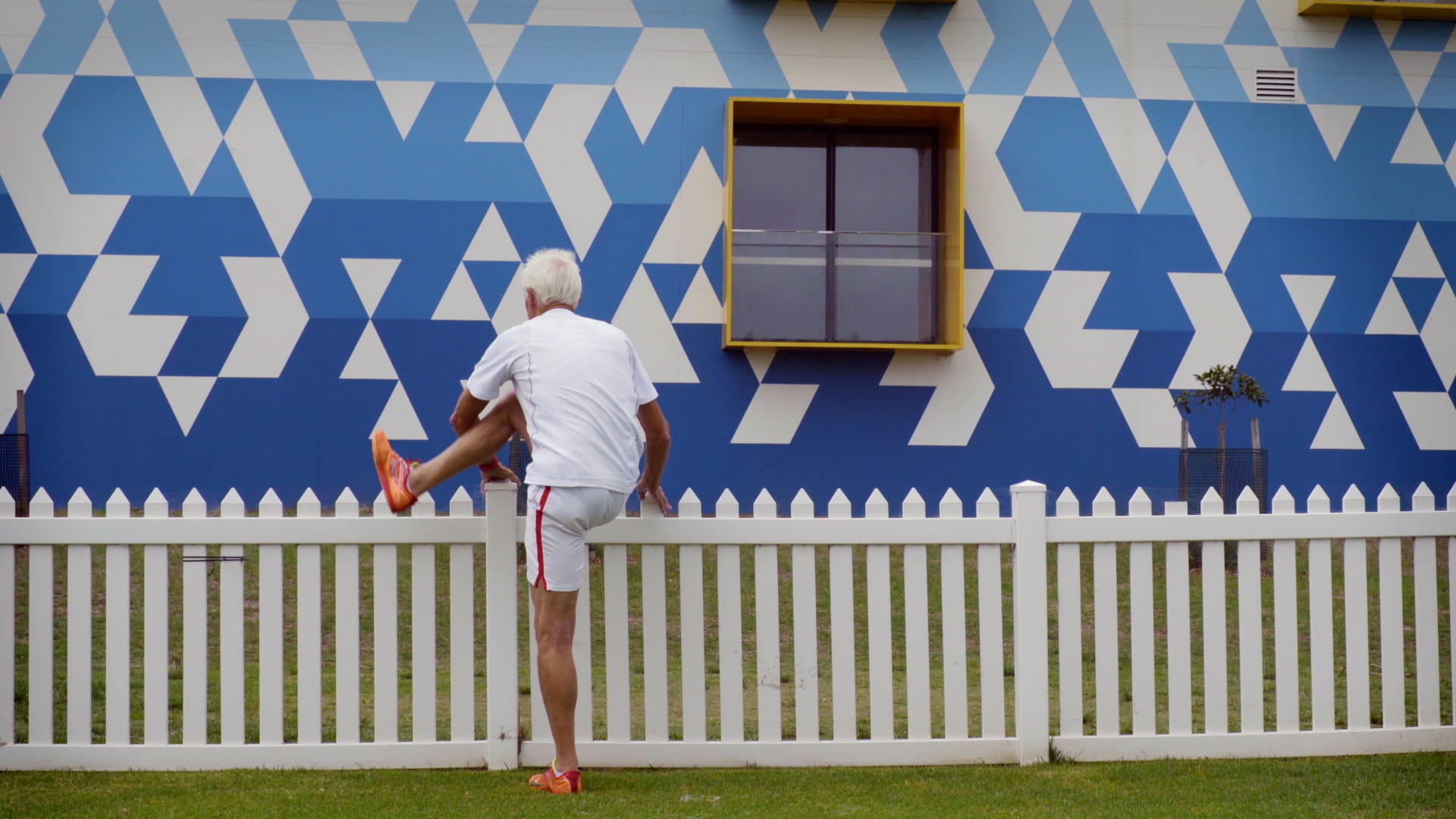 Sports photography Older man stretches against a white picket fence.