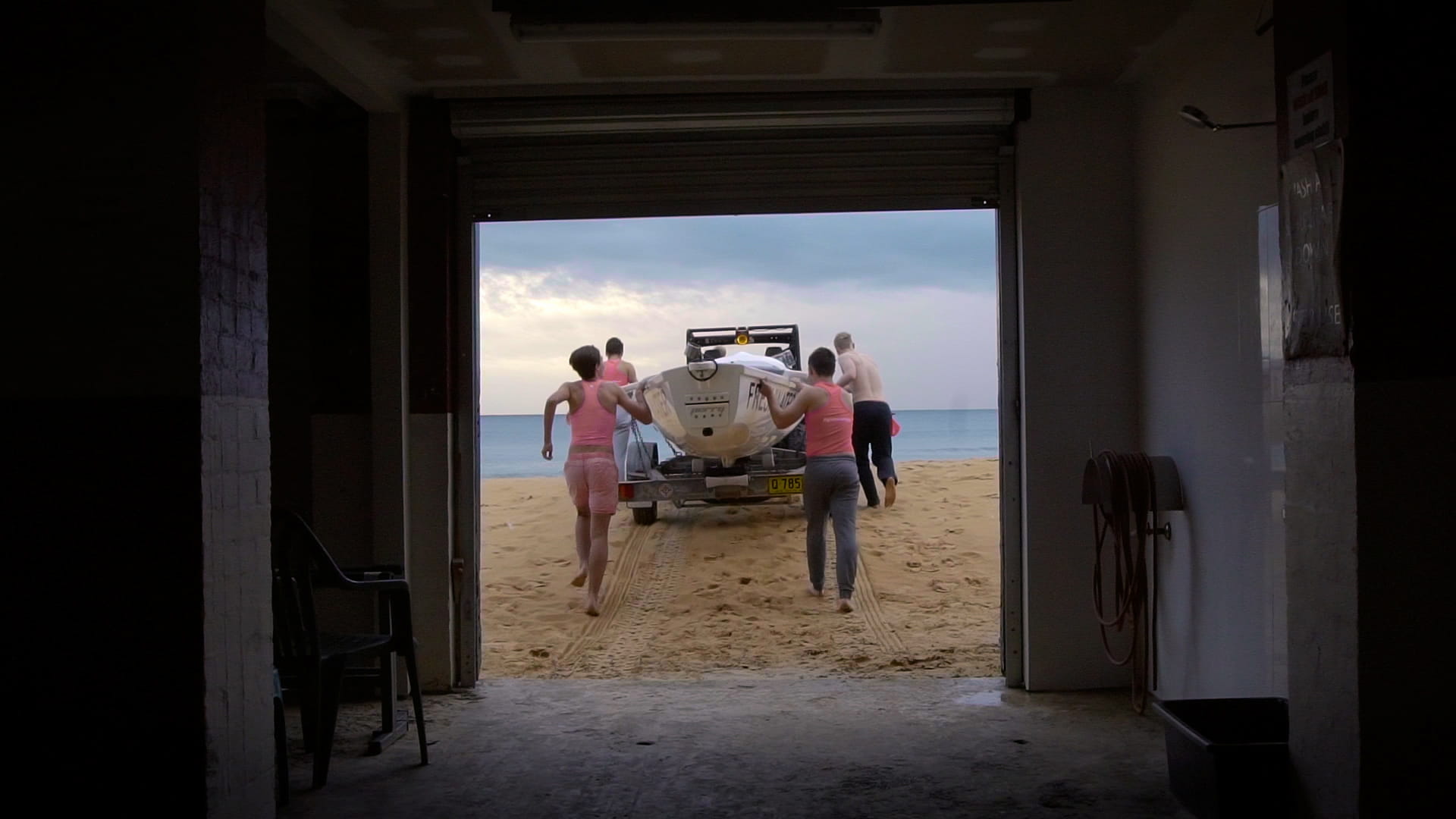 Australian beach sports Four men pushing a row boat out from a garage onto the beach.