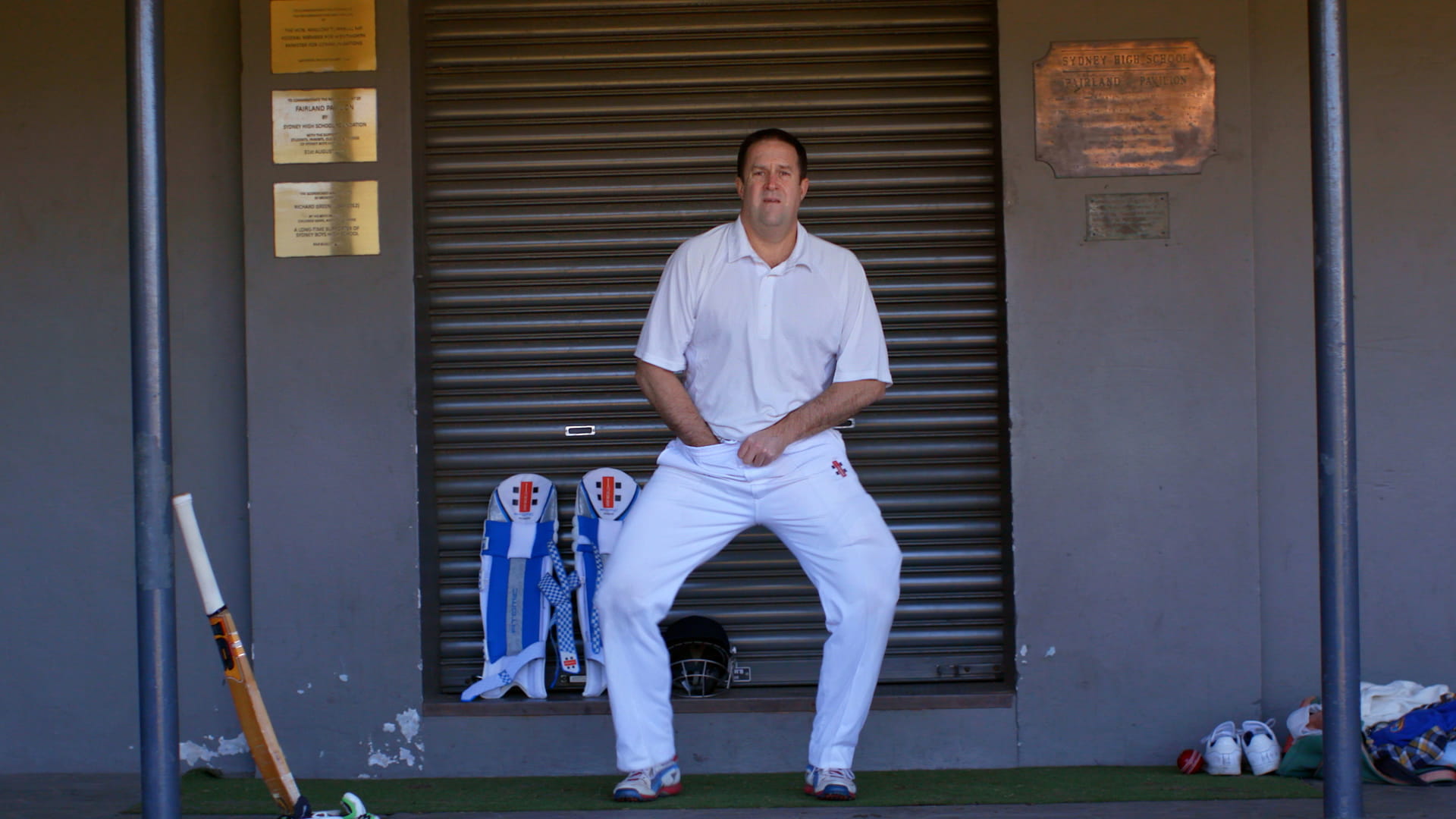 Cricketer Male cricketer adjusting his box next to a Sydney Highschool plaque.