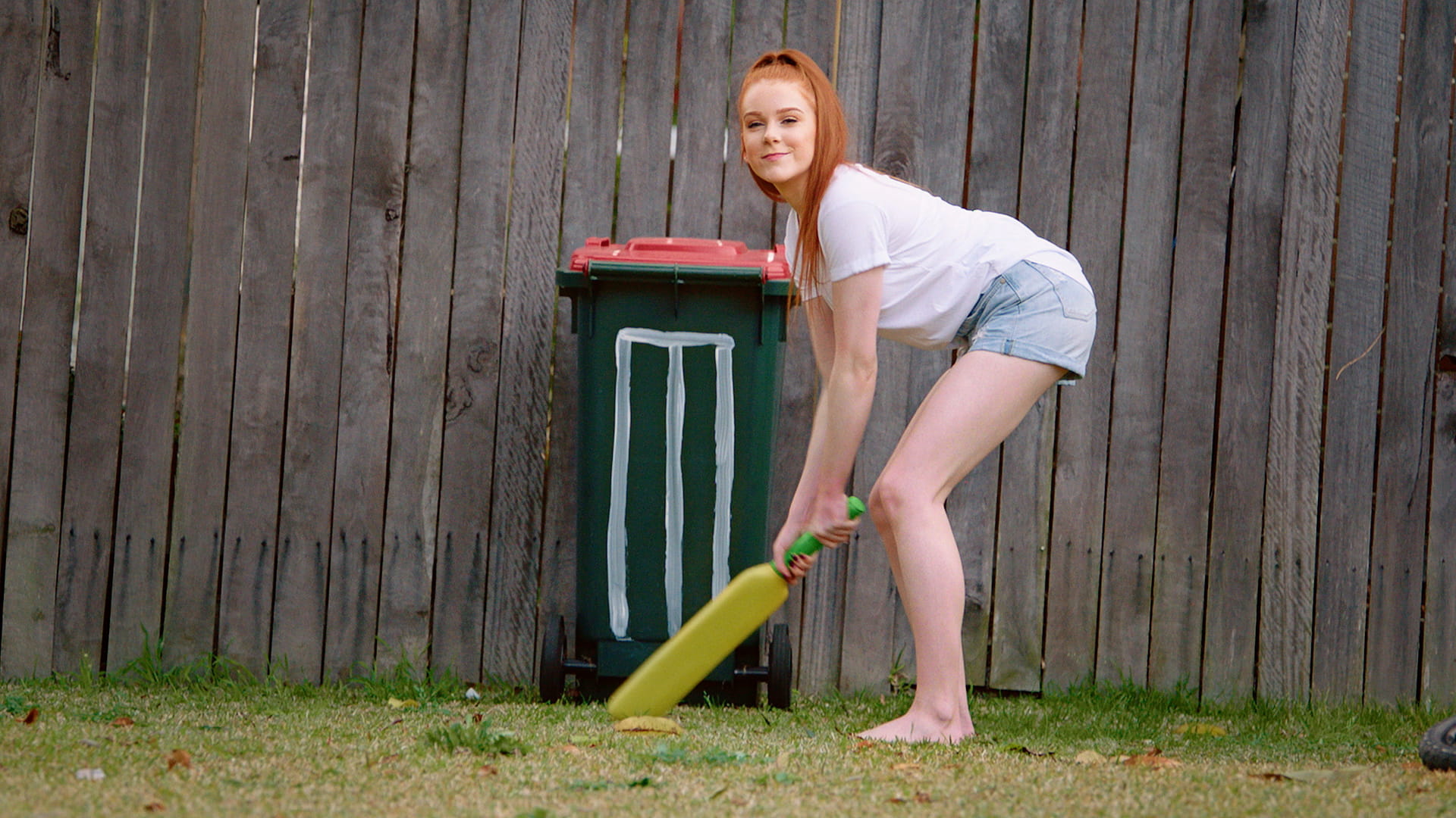 Backyard cricket Woman with cricket bat assuming batting stance in front of stumps drawn on a garbage bin.