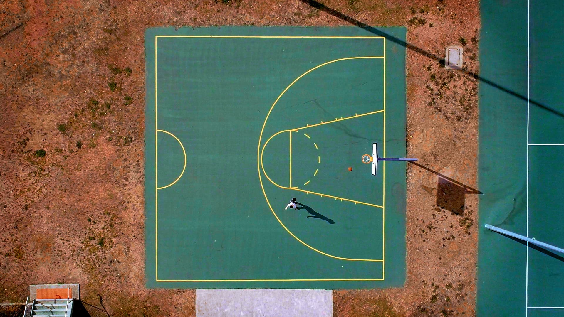 Basketball drone shot Aerial top-down shot of lone person on a basketball half-court shooting hoops.