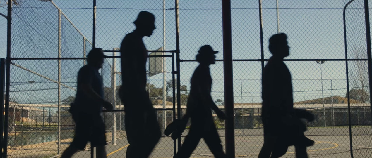Shakespearean documentary Four silhouettes of boys walking past basketball court.