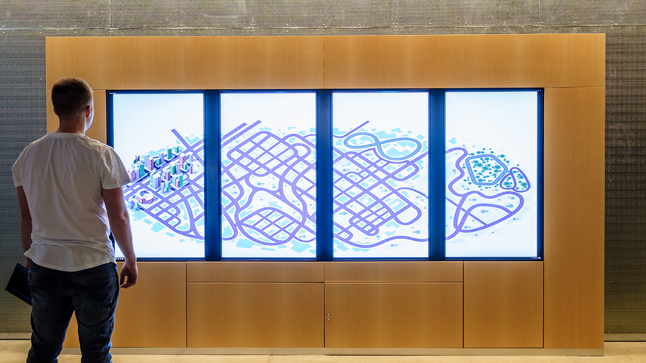 Data visualisation exhibition Wideshot of Road to Zero foyer activation, four vertical screens displaying a large stylised cityscape.
