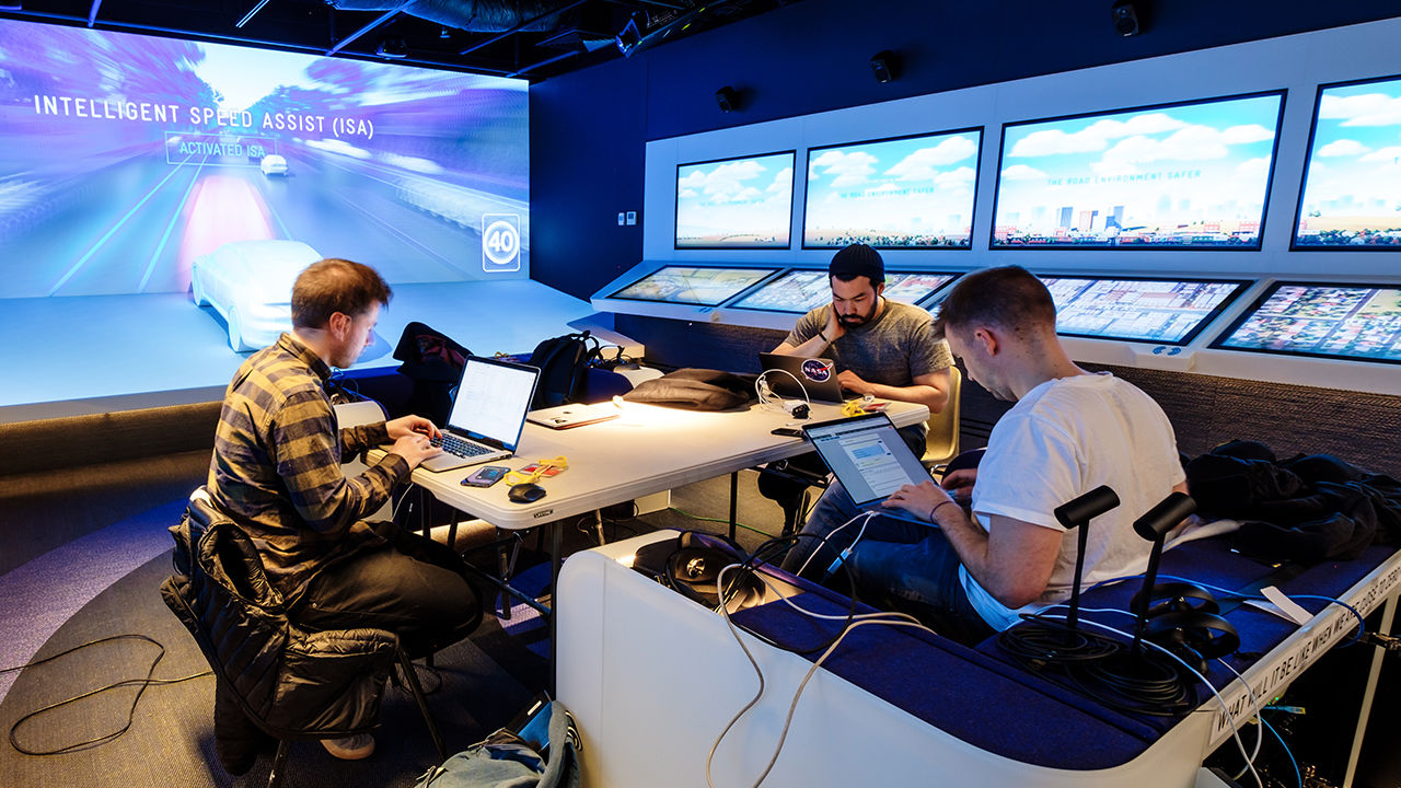 Three men on laptops gathered around a desk.