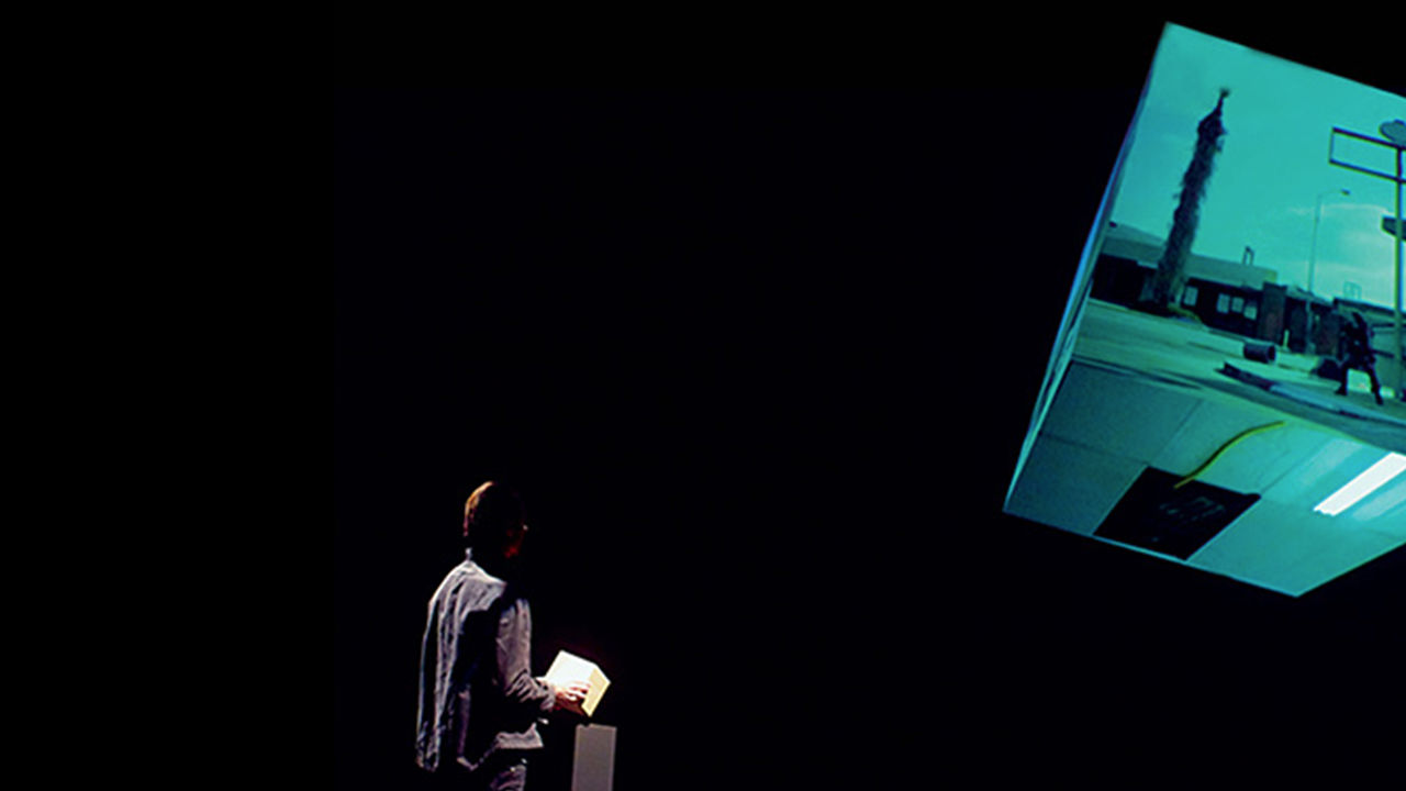 Interactive film experience Man holding The Cube, interacting with video played on a larger 3D projected cube.